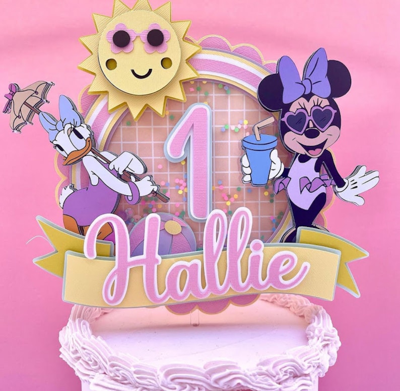 K&ouml;nnte beinhalten: Ein rosa und gelber Tortendekor mit einer Sonne, einer Nummer eins, einem Strandball, einer Minnie Mouse Figur mit Sonnenbrille und einem lila Badeanzug und einer Donald Duck Figur mit einem lila Badeanzug. Der Topper enth&auml;lt auch ein gelbes Banner mit dem Namen "Hallie" in rosa.