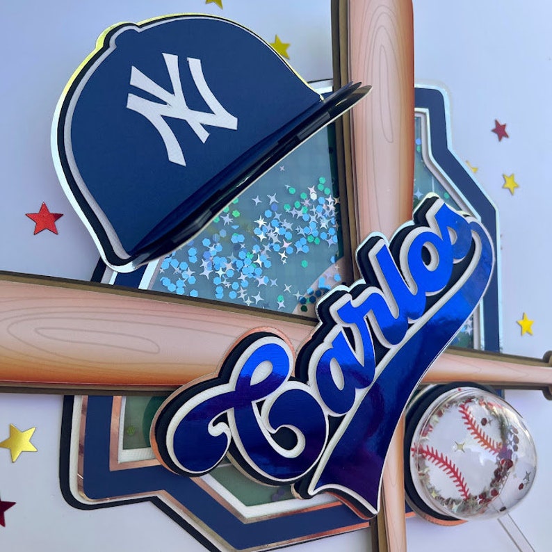 Pu&ograve; includere: Un cappello da baseball blu e bianco con una mazza da baseball e il nome "Carlos" in scrittura blu. Lo sfondo &egrave; un campo da baseball con glitter.