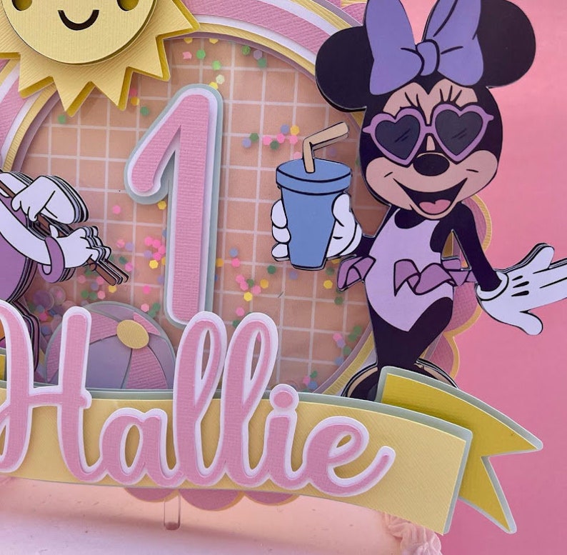 K&ouml;nnte beinhalten: Ein rosa und gelber Tortendekor mit einer Comicfigur, die eine Sonnenbrille und einen Badeanzug tr&auml;gt, der Zahl eins und dem Namen "Hallie".