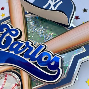 Pu&ograve; includere: Un topper per torta a tema baseball blu e bianco con il nome "Carlos" in scrittura blu. Il topper presenta una mazza da baseball, un cappello da baseball e una palla da baseball.