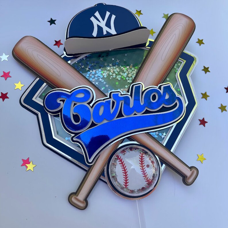 Pu&ograve; includere: Un cappello da baseball blu e bianco con una mazza da baseball e una palla da baseball. Il nome Carlos &egrave; scritto in lettere corsive blu su uno sfondo blu e argento. Lo sfondo &egrave; ricoperto di glitter.