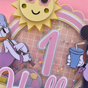 K&ouml;nnte beinhalten: Eine rosa und wei&szlig;e mehrst&ouml;ckige Torte mit einer Sonne, einer Eins und einer Mickey-Maus-Figur. Die Torte ist mit bunten Streuseln und einem rosa-wei&szlig;en Karomuster verziert.