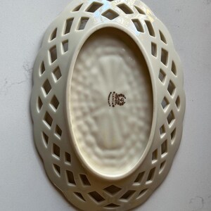 May include: Cream-colored, oval-shaped Lenox dish with a lattice design around the rim. The interior has a textured pattern and a Lenox stamp. The dish is made of porcelain.