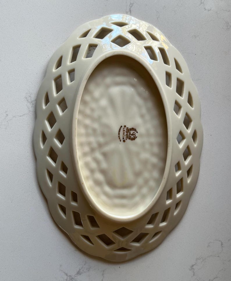 May include: Cream-colored, oval-shaped Lenox dish with a lattice design around the rim. The interior has a textured pattern and a Lenox stamp. The dish is made of porcelain.