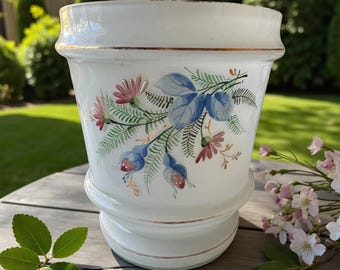 May include: White ceramic planter with a floral design in blue, pink, and green. The planter has a gold rim and a decorative base. The floral design features stylized flowers and leaves. The planter is suitable for indoor or outdoor use.