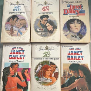 May include: A collection of six vintage paperback books by Janet Dailey. The covers feature illustrations of couples, landscapes, and the titles "The Travelling Kind", "Northern Magic", "Savage Land", "Dangerous Masquerade", "The Bride of the Delta Queen", and "Night of the Cotillion".