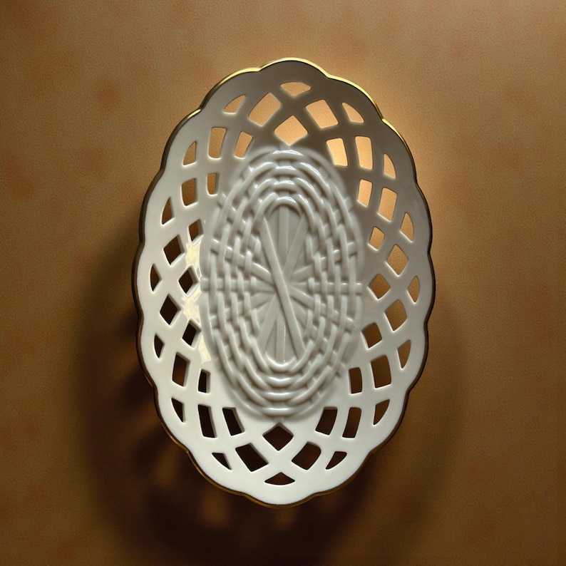 May include: White oval-shaped ceramic basket with a lattice design and a gold trim. The basket has an open weave pattern, allowing light to pass through. The interior features a woven texture.