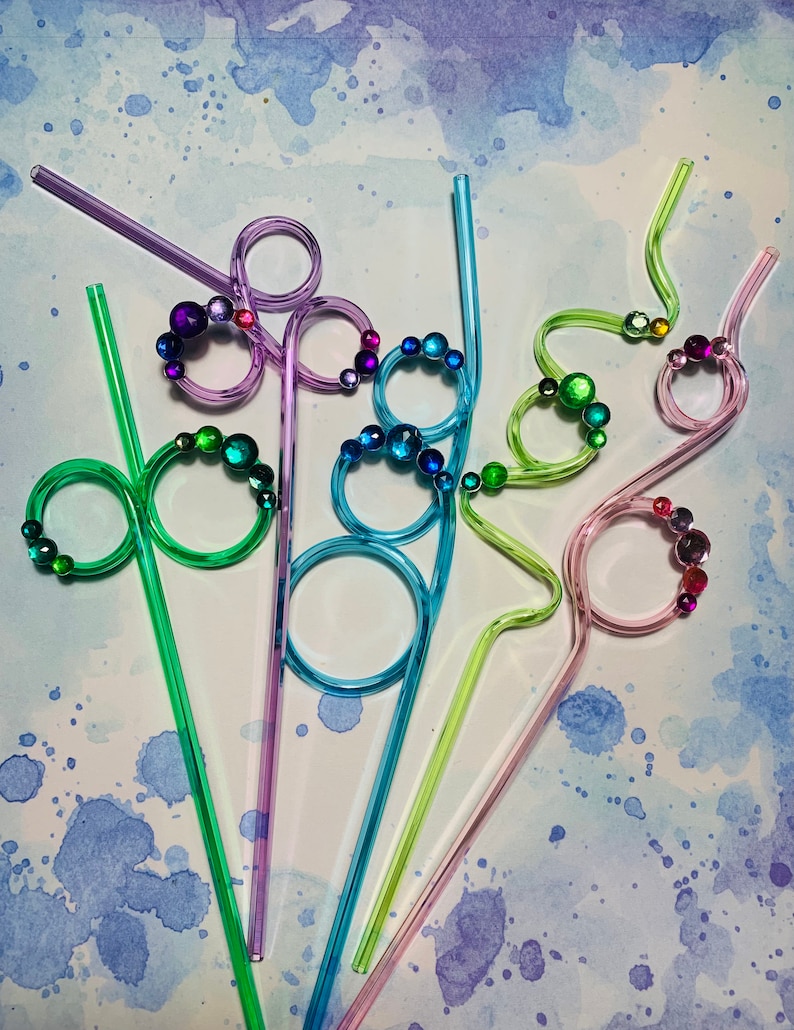 Puede incluir: Cinco pajitas para beber de colores con detalles decorativos de joyas. Las pajitas son de pl&aacute;stico y tienen diferentes formas y dise&ntilde;os. Las pajitas est&aacute;n dispuestas en forma de abanico sobre un fondo azul claro.