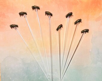 Puede incluir: Ocho palitos de vidrio transparente con una mosca en la parte superior de cada palito. Las moscas son de diferentes colores y tienen un aspecto realista.