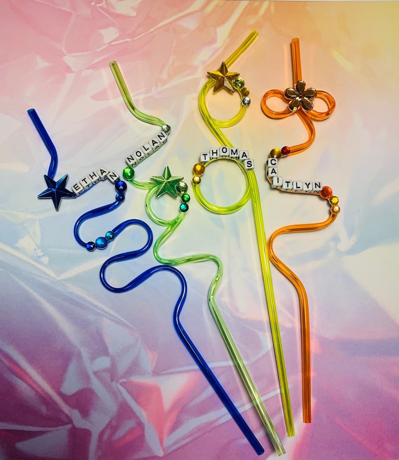 Puede incluir: Cuatro pajitas flexibles de colores con nombres personalizados escritos en cuentas de letras blancas. Las pajitas est&aacute;n decoradas con estrellas y un amuleto de flor.