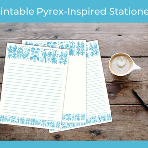 May include: Three sheets of white stationery paper with blue lines and a blue patterned border. The border features a stylized design of a rooster, flowers, and other folk art motifs. The paper is on a wooden surface.
