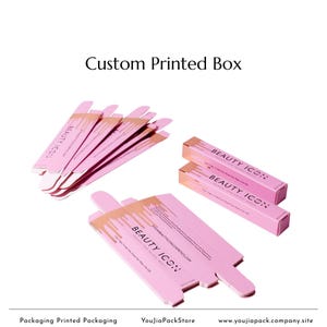 May include: Pink custom printed boxes with gold accents and the text "BEAUTY ICON". The boxes are for packaging and display the brand's name and website. The image shows several boxes, some folded and some flat.