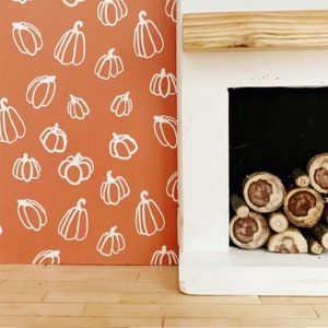 May include: A white fireplace with a black opening and a stack of firewood inside. The fireplace is against a wall with an orange background and a white pumpkin pattern.