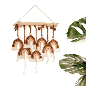 May include: A macramé rainbow wall hanging with seven arches in brown and cream hues, suspended from a natural wood branch. Each rainbow has a fringe and crystal accents. Ideal for home decor, this piece adds a touch of bohemian style.