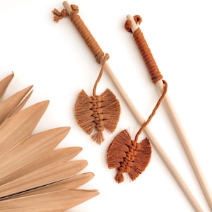 Peut inclure: Deux bâtonnets en bois enroulés de fil brun. Chaque bâtonnet est doté d'un pompon brun à son extrémité. Les pompons ont la forme d'un cœur.