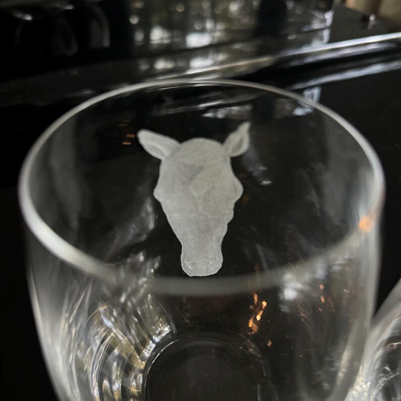Puede incluir: Un vaso de vidrio transparente con un dise&ntilde;o grabado de una cabeza de caballo. El vaso est&aacute; vac&iacute;o y parece ser parte de un juego.