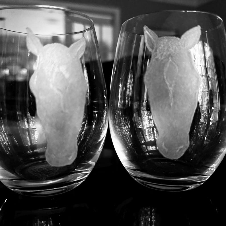 Puede incluir: Dos copas de vino de vidrio transparente con dise&ntilde;os de cabeza de caballo grabados.