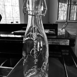 May include: A clear glass bottle with a metal swing top lid. The bottle is etched with musical notes and the text "The House of the Music".