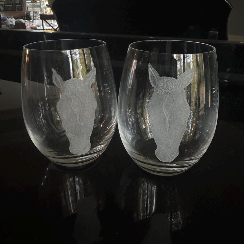 Puede incluir: Dos copas de vino de vidrio transparente con dise&ntilde;os de cabeza de caballo grabados.