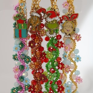 May include: Four Christmas-themed beaded keychains with gold-colored clasps. Each keychain features a different charm: a wrapped gift, a dog in a Santa hat, the Grinch, and Cindy Lou Who. The beaded strands are in various colors.
