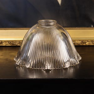 May include: A clear glass lamp shade featuring a dome shape with vertical ribbed detailing and a scalloped edge. The shade has a circular opening at the top for mounting, with a transparent finish that allows light to pass through the textured surface.