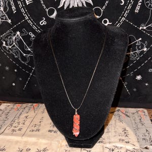 May include: A silver chain necklace with a red and white spiral crystal pendant.