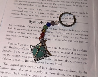 Op de afbeelding: Een sleutelhanger met een zilverkleurige metalen ring bevestigd aan een reeks kleine, veelkleurige bolvormige kralen in paars, blauw, groen, bruin en rood, eindigend in een groene bolvormige steen in een geometrische metalen kooi.
