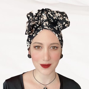 Może przedstawiać: Czarny turban w kwiaty w kolorze kremowym i beżowym jest noszony. Osoba nosi również czarne kolczyki i czarny naszyjnik z wisiorkiem z prostokątnym czarnym kamieniem. Osoba ma na sobie czarny top.