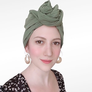 Peut inclure: Une femme portant un turban vert en tissu avec des boucles d'oreilles en or. Elle porte un haut à imprimé floral noir et blanc.