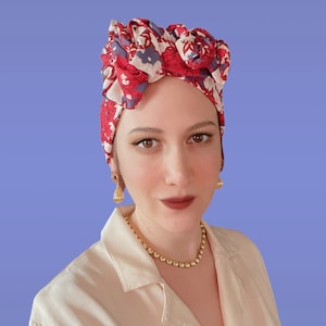 Può includere: Una donna indossa un turbante a stampa floreale rosso e blu con orecchini dorati e una collana a catena dorata.