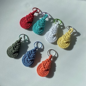 May include: Seven colorful rope keychains with a knot design. The keychains are red, teal, white, yellow, green, blue, and orange.