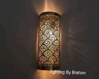 May include: A gold metal wall sconce with a cylindrical shade featuring a decorative pattern of overlapping circles. The light is on and casting a warm glow.