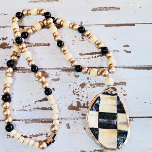 May include: A black and white checkered oyster shell pendant necklace with gold and cream colored beads.