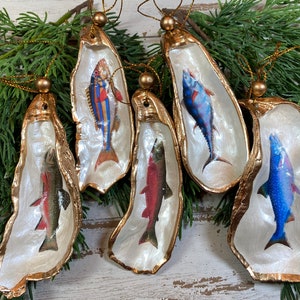 May include: Five gold-rimmed oyster shell ornaments with different fish illustrations. The fish are painted in shades of blue, red, and green.