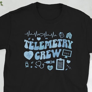 May include: Black t-shirt with the words "Telemetry Crew" in light blue, along with medical-themed graphics. The design includes a heartbeat line, a heart, a hospital, and other medical symbols. A stylish and comfortable tee.