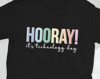 May include: Black t-shirt featuring the word "HOORAY!" in pastel shades. Underneath, the text reads "it's technology day" in a cursive style. The tee-shirt has a round neck and short sleeves.