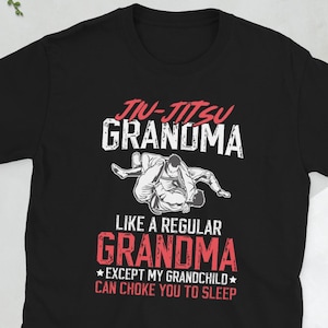 Könnte beinhalten: Schwarzes T-Shirt mit dem Text "Jiu-Jitsu Grandma" in Weiß und Rot, mit einer Grafik von zwei Personen in einer Kampfsport-Position. Der Text darunter lautet: "Wie eine normale Oma, außer mein Enkel kann dich in den Schlaf würgen."