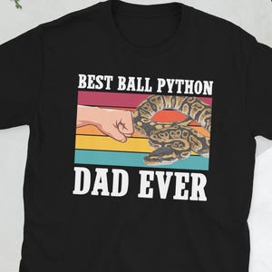 Peut inclure: T-shirt noir avec l'inscription blanche "BEST BALL PYTHON DAD EVER". Le graphisme représente un "high five" avec un python royal et un fond coloré de rayures rouges, orange, jaunes et bleues. Un cadeau idéal pour un passionné de reptiles.