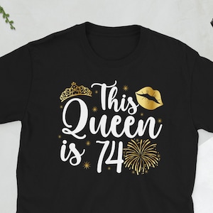 Puede incluir: Camiseta negra con texto blanco que dice "This Queen is 74" con una corona dorada, labios y un gráfico de fuegos artificiales.