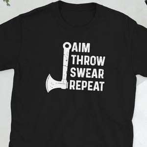 May include: Black t-shirt with the words "AIM THROW SWEAR REPEAT" in white, along with a white axe graphic. The shirt is a short-sleeved crew neck style.
