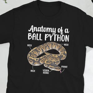 Puede incluir: Camiseta negra con una ilustración detallada de una pitón real y su anatomía. El texto "Anatomy of a Ball Python" está impreso encima de la imagen de la serpiente. La serpiente es marrón y beige con un contorno negro.