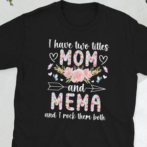 Könnte beinhalten: Schwarzes T-Shirt mit dem Text "I have two titles MOM and MEMA and I rock them both". Der Text ist in Weiß, Rosa und floralen Mustern gehalten. Das Shirt hat einen Rundhalsausschnitt und kurze Ärmel.