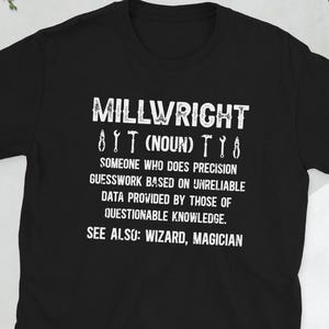 Op de afbeelding: Zwart T-shirt met witte tekst die luidt: "MILLWRIGHT 8T (NOUN) TY SOMEONE WHO DOES PRECISION GUESSWORK BASED ON UNRELIABLE DATA PROVIDED BY THOSE OF QUESTIONABLE KNOWLEDGE. SEE ALSO: WIZARD, MAGICIAN"