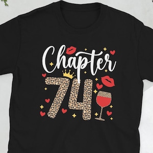 Puede incluir: Camiseta negra con el texto "Chapter 74" en blanco con un diseño de estampado de leopardo. El número 74 está decorado con una corona y una copa de vino.