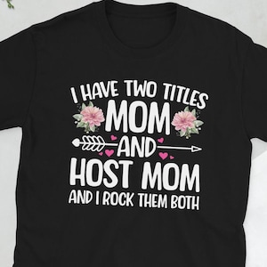 May include: Black t-shirt with white text that reads "I have two titles Mom and Host Mom and I rock them both". The text is surrounded by pink flowers and an arrow with pink hearts.