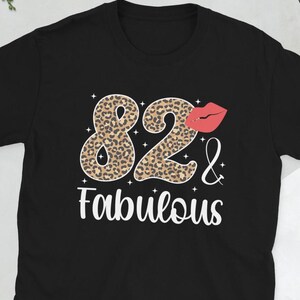 May include: Black t-shirt with a leopard print design of the number 82 and the text "& Fabulous". A red lip print is above the number 2.
