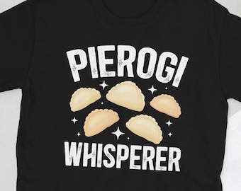 以下が含まれることがあります： 「Pierogi Whisperer」という白い文字と、5つのピエロギのグラフィックが描かれた黒いTシャツです。