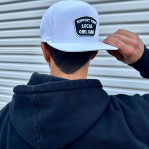 Può includere: Cappellino da baseball bianco con una toppa nera che dice "Support Your Local Girl Dad".