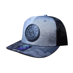 Può includere: Un cappello da camionista grigio e nero con un logo ricamato nero che dice "Dadbod Apparel" con una "D" e una "B" barrate. Il cappello ha una parte posteriore in rete nera e una visiera con motivo mimetico.