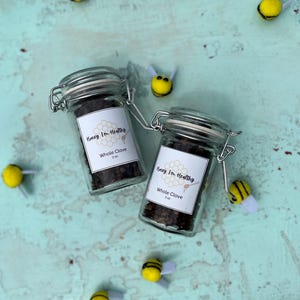 May include: Two glass jars filled with whole cloves, each with a label that reads "Honey I'm Healthy" and "Whole Clove 2 oz." The jars are surrounded by yellow and black bee decorations on a light blue surface.